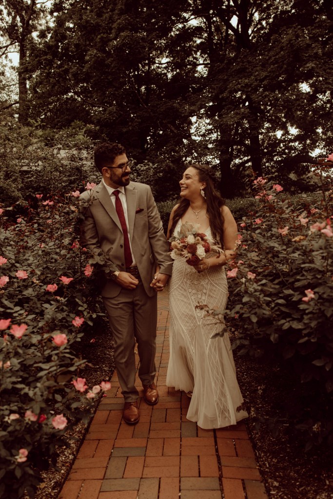 bride and groom walk through rose bushes frelinghuysen arboretum